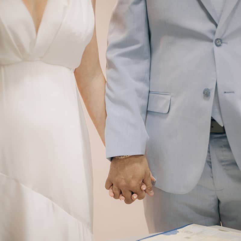 Noiva de vestido branco com decote em V de mãos dadas com o noivo no cartório, casamento civil