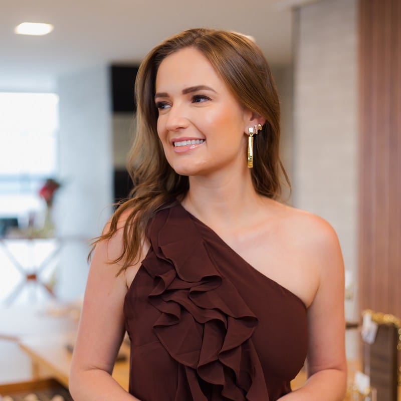 Mulher sorrindo de vestido marsala um ombro só com brinco dourado e pulseiras douradas: acessórios para madrinha e convidada de casamento