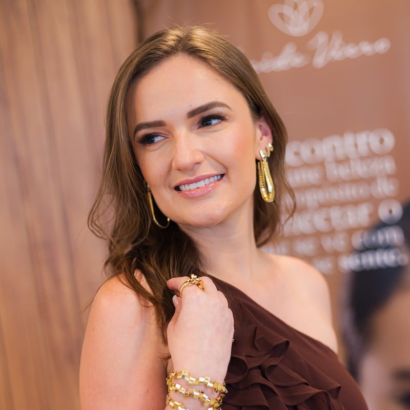 Mulher sorrindo de vestido marsala com brinco pendente, anel e pulseiras douradas: o que os acessórios dizem sobre você