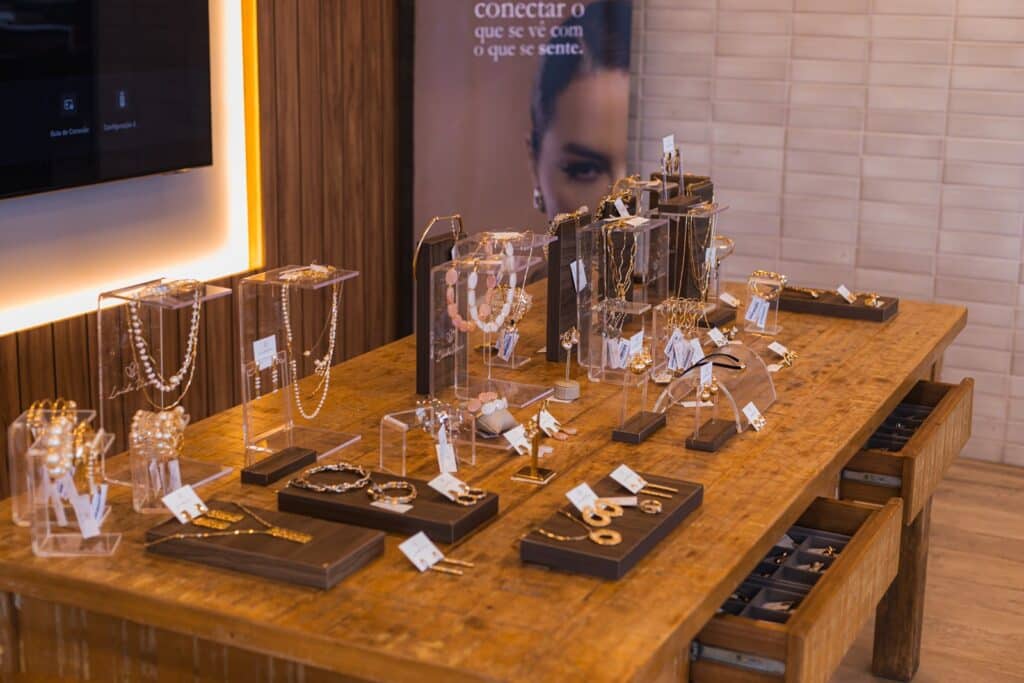 Mesa de madeira do ateliê Leide Viero com colares, brincos e pulseiras expostos em suportes de acrílico